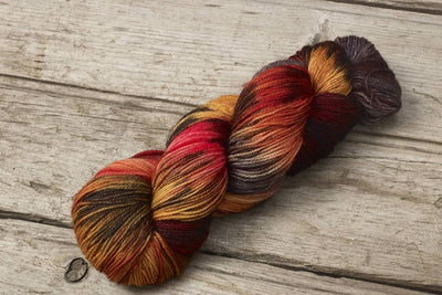Hand dyed multiple Autumn colour hues yarn by Alegria Yarn by Manos del Uruguay. 75% Superwash Merino Wool, 25% Polyamide (Nylon) for durability. Multicolored skein of yarn on a wooden surface