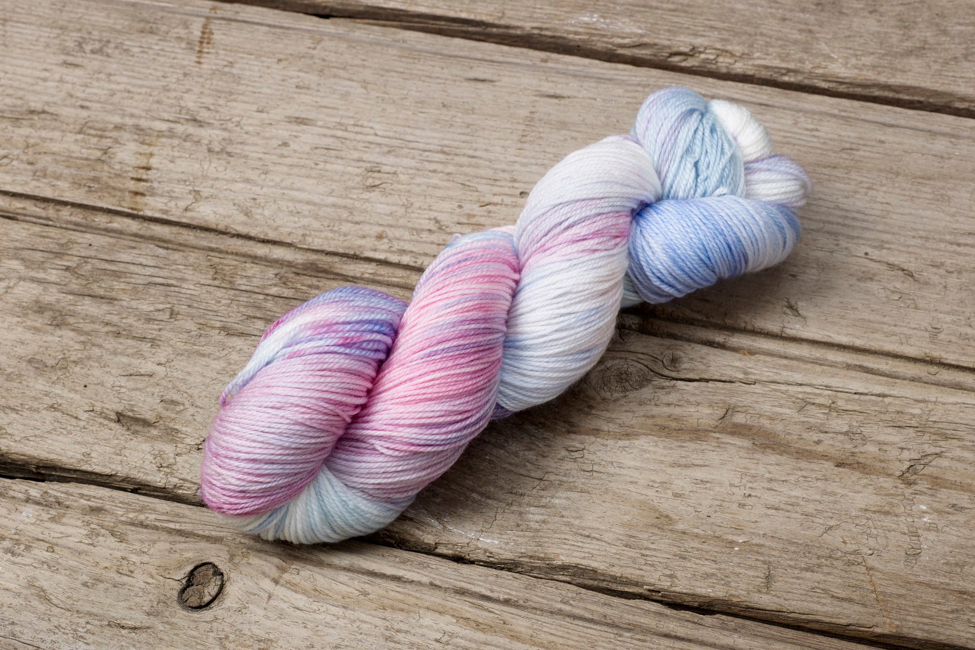 Hand dyed multiple pastel colour hues yarn by Alegria Yarn by Manos del Uruguay. 75% Superwash Merino Wool, 25% Polyamide (Nylon) for durability. Pastel skein of yarn on a wooden surface
