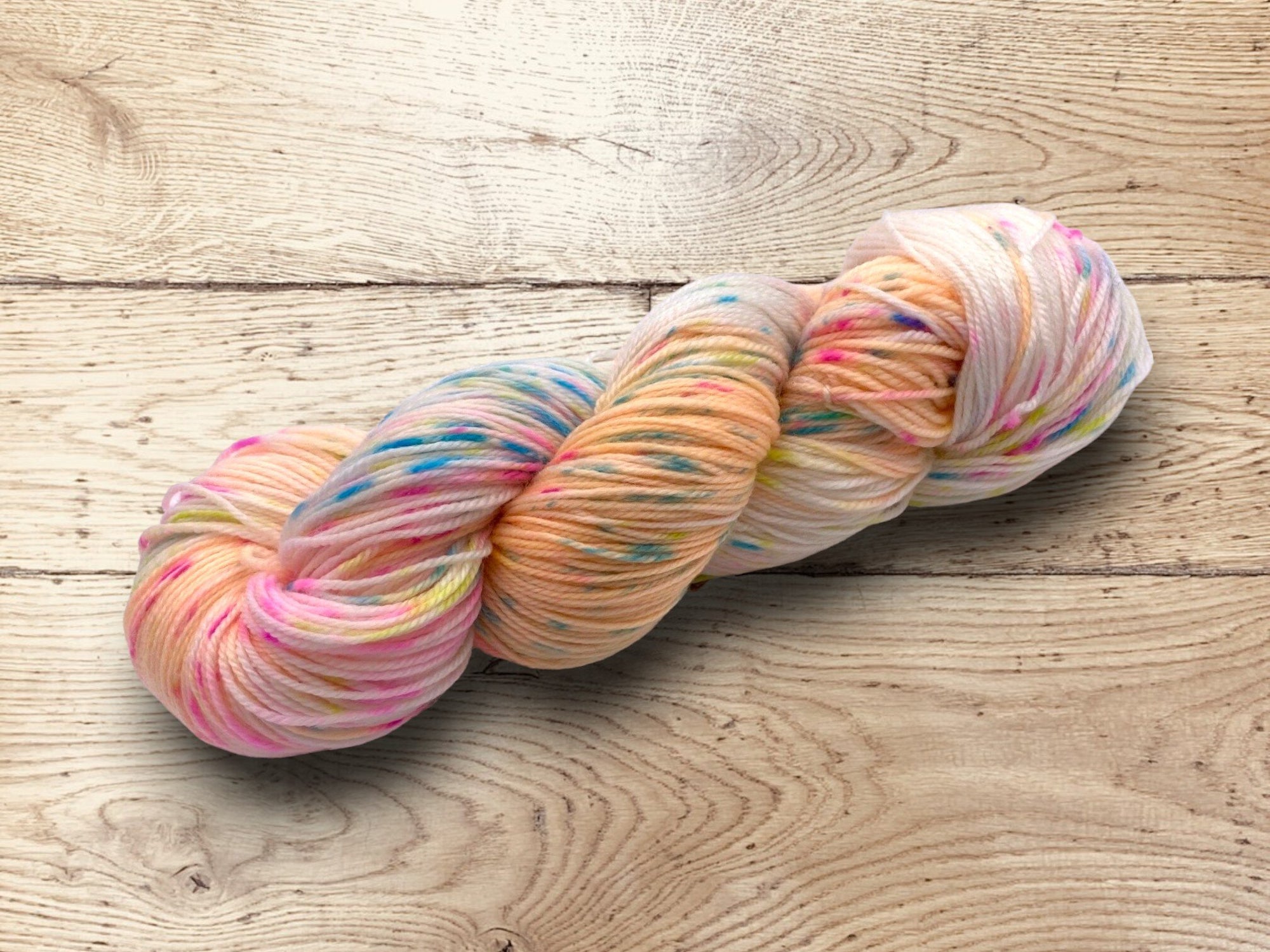 Hand dyed multiple colour hues yarn by Alegria Yarn by Manos del Uruguay. 75% Superwash Merino Wool, 25% Polyamide (Nylon) for durability. Multicolored skein of yarn on a wooden surface