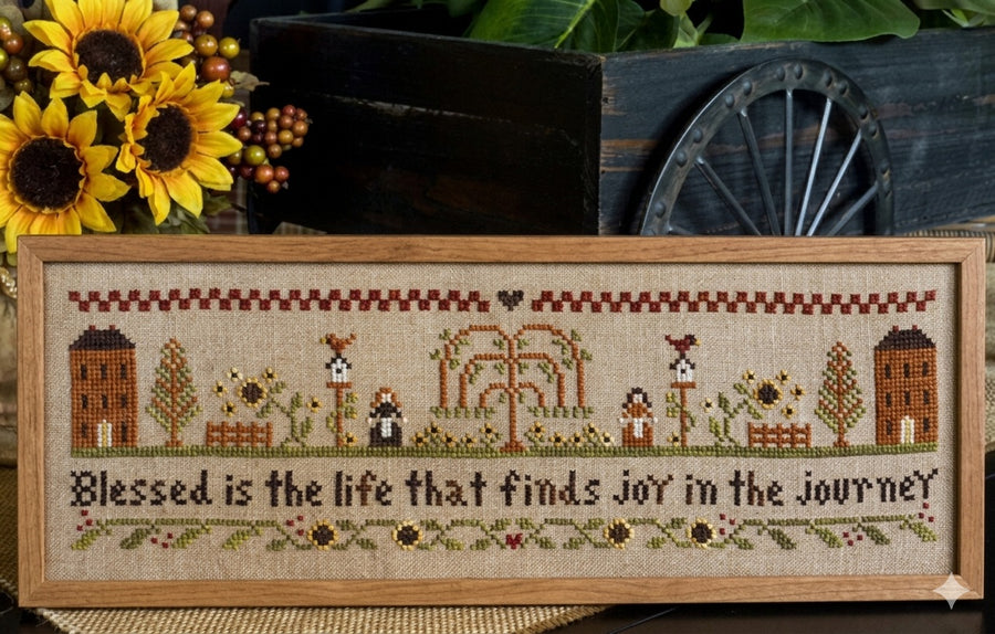 "A professional cross-stitch chart for an inspirational sampler titled 'Blessed is the Life.' The design features the horizontal text 'Blessed is the life that finds joy in the journey' rendered in elegant, artisanal typography. The lettering is surrounded by delicate, high-definition floral or border motifs in a classic folk-art style
