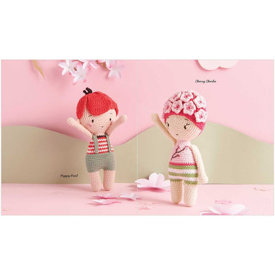Two crochet dolls with red hair and floral headband on a pink background