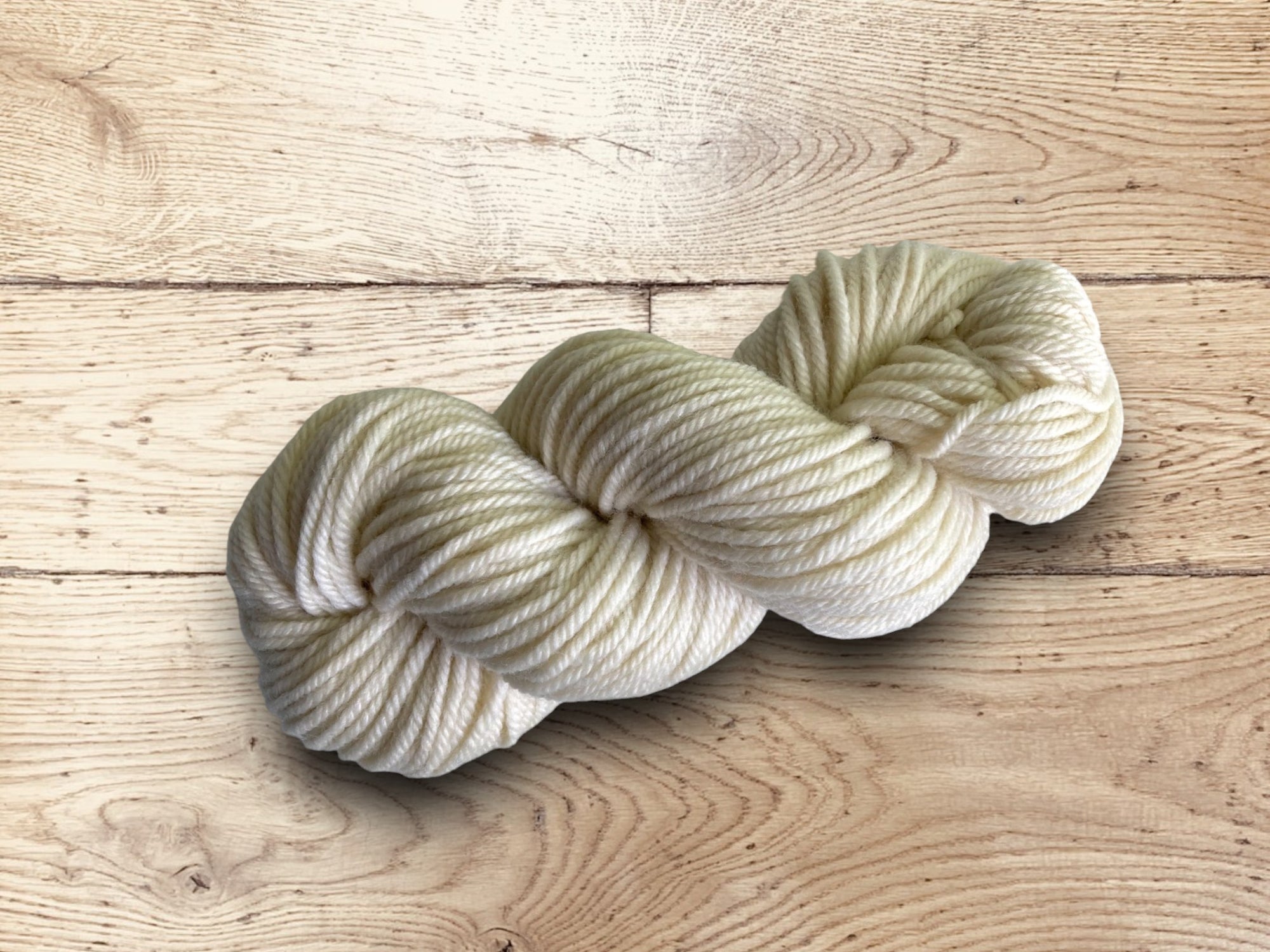Chunky cream-colored yarn on a wooden surface.100% Uruguayan Corriedale chunky yarn for sale.