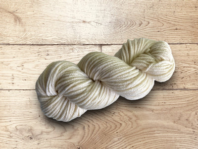 Chunky cream-colored yarn on a wooden surface.100% Uruguayan Corriedale chunky yarn for sale.