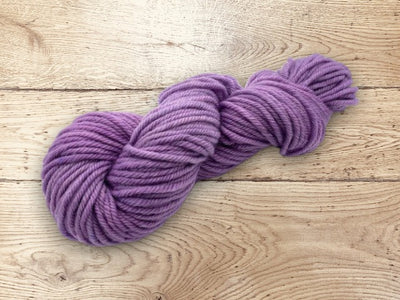 Purple skein of 100% non-superwash Corriedale wool yarn on a wooden surface.