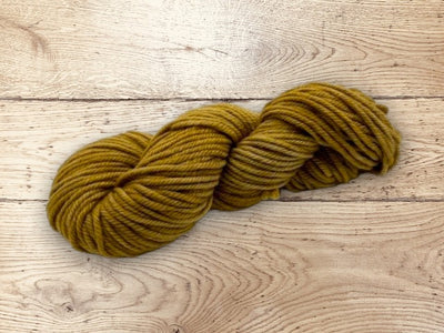 Mustard yellow-brownish yarn skein on a wooden surface. 100% Uruguayan Corriedale yarn for sale
