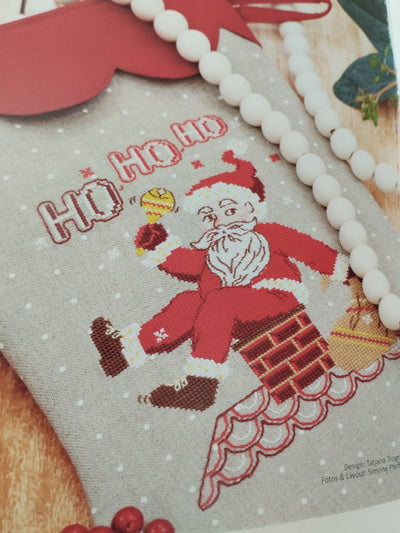 Cross-stitched design of Santa Claus on a fabric background with 'Ho Ho Ho' text.