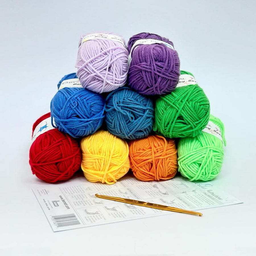 A vibrant and cheerful rainbow crochet starter kit featuring nine 50g balls of 100% acrylic yarn in a full spectrum of colors, including bright red, sunny yellow, deep blue, and vivid purple. The kit includes a premium Japanese Tulip double-sided crochet hook (3.0mm/3.5mm) and an English instruction guide, presented as a perfect gift set for new crafters.