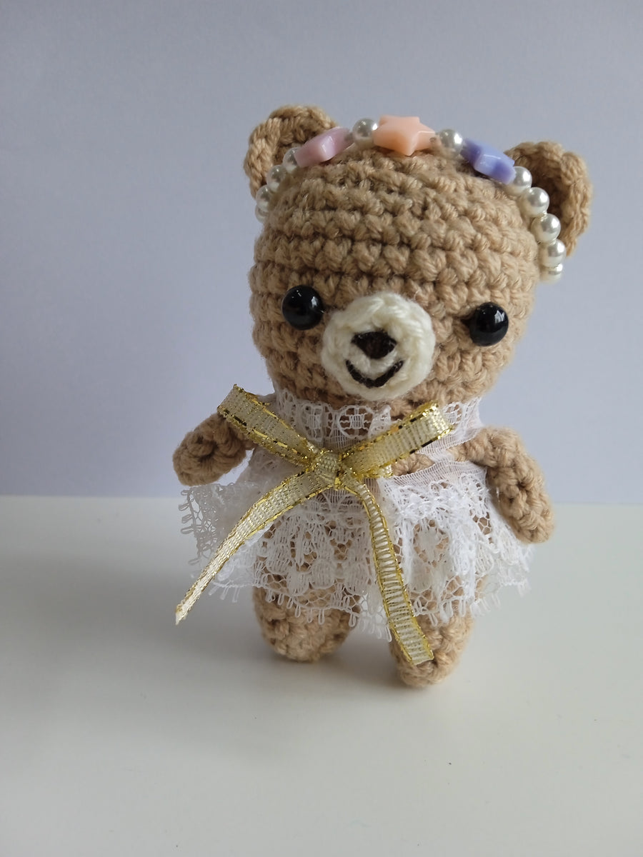 Crocheted teddy bear in a white lacy dress with a gold bow. Stuffed animal photography. travel companion Instagrammable photo.
Handmade Fig and Friends crocheted bear. the perfect palm-sized traveling companion made from soft, durable yarn for comfort on long journeys.