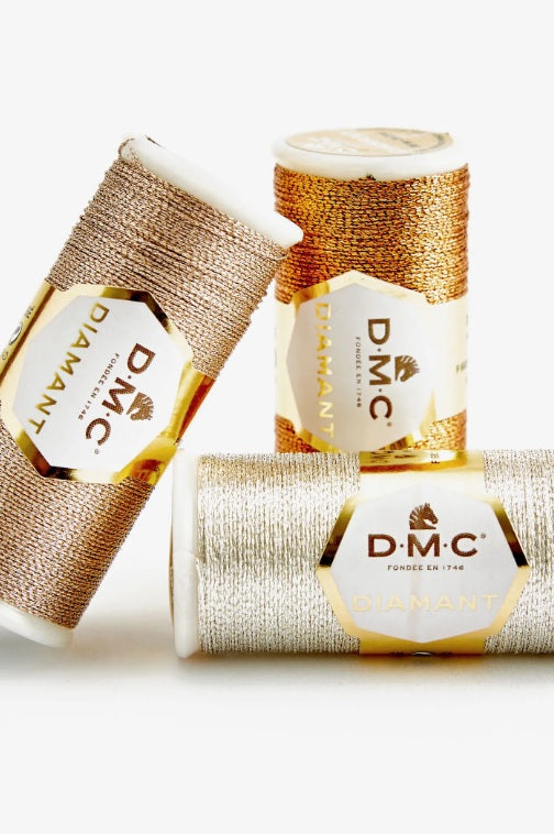 Three spools of DMC thread with gold and white packaging on a white background
