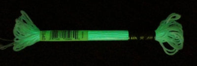 A high-quality skein of DMC Light Effects Glow in the Dark embroidery thread, color code E940. This artisanal thread appears as a soft, brilliant white in daylight but emits a delicate luminous green glow in the dark after exposure to light glow in the dark effect
