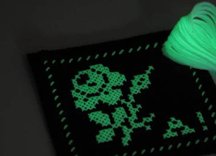 Glowing green cross-stitch design on fabric with a spool of thread.