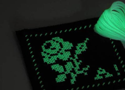 Glowing green cross-stitch design on fabric with a spool of thread.