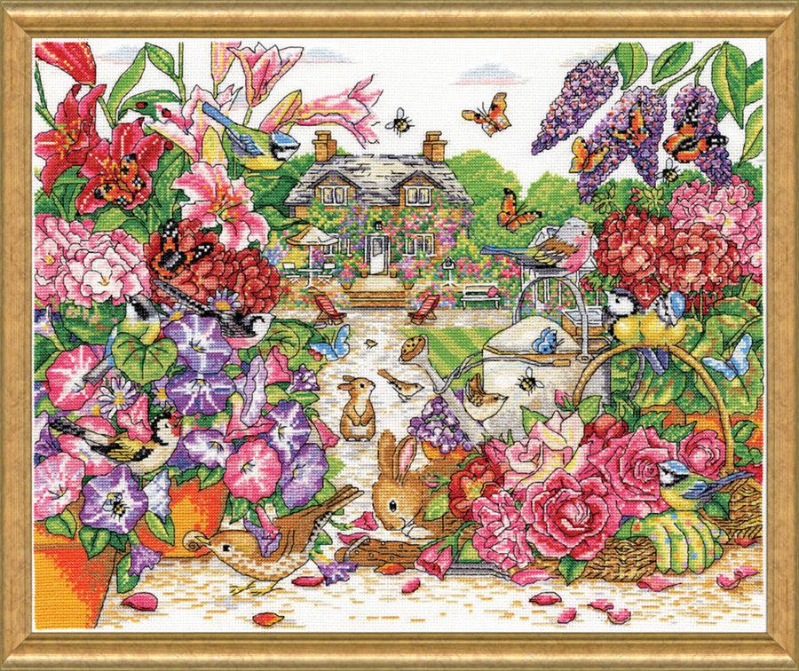 A large-scale Design Works counted cross-stitch kit titled 'Full Bloom Garden' by artist Joan Elliott. The artwork depicts a dense, vibrant garden filled with pink, purple, and eggplant-colored flowers, featuring hidden rabbits, bees, and butterflies. The kit is shown with 14-count white Aida fabric, a pre-sorted thread palette of 100% cotton floss, a needle, and a detailed pattern chart.