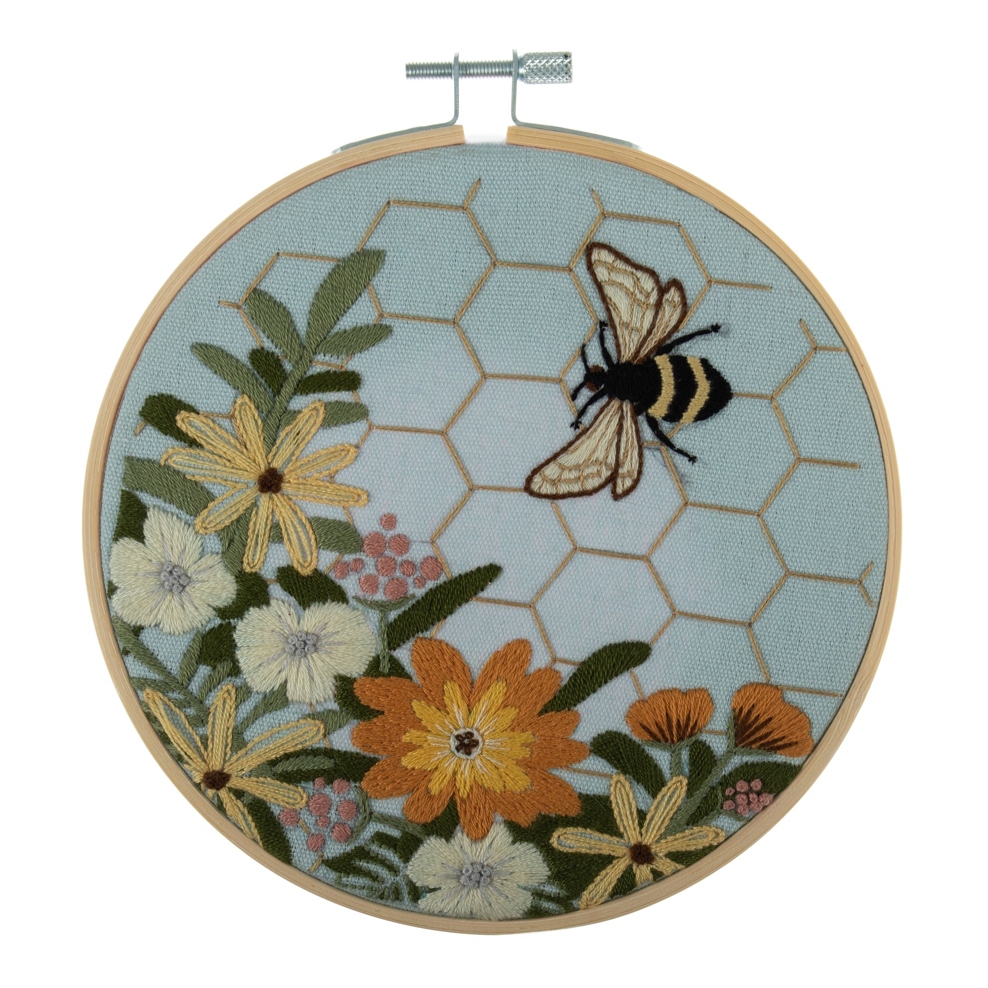 Embroidery hoop kit depicting a floral design with bee motifs and a honeycomb pattern on a light blue background, completed and framed.