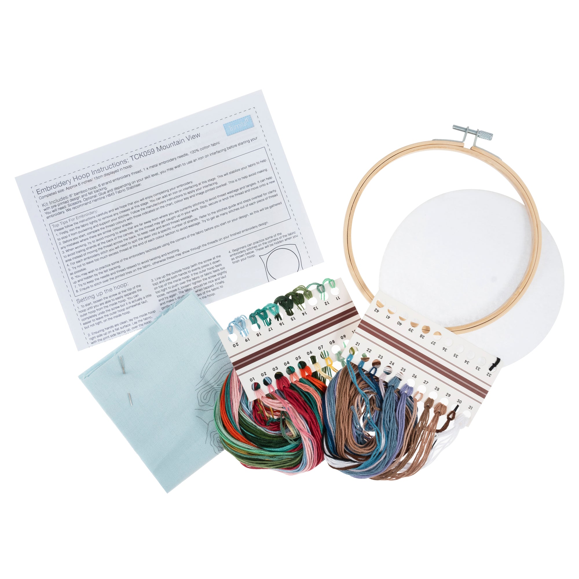 Flat-lay of the mountain kit: 10-inch pre-printed fabric, earthy-toned embroidery threads in blues and greys, bamboo hoop, needle, and felt backing