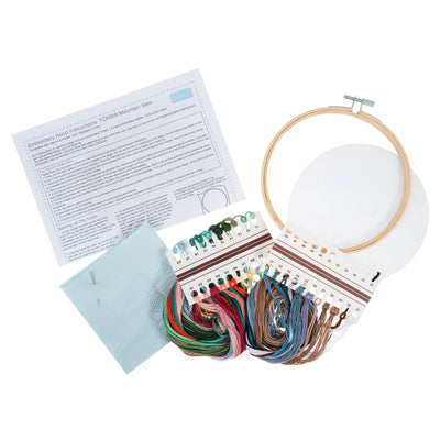 Flat-lay of the mountain kit: 10-inch pre-printed fabric, earthy-toned embroidery threads in blues and greys, bamboo hoop, needle, and felt backing
