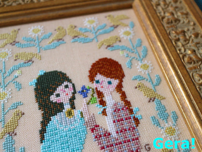 Cross-stitched picture of two women with birds and flowers, framed in gold. Inspired by Anne of Green Gables and her bosom friend Diana Barry.