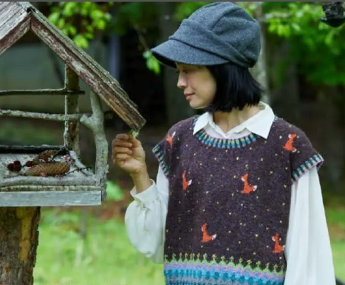Person wearing a patterned knitted sweater and cap, interacting with a bird feeder outdoors.