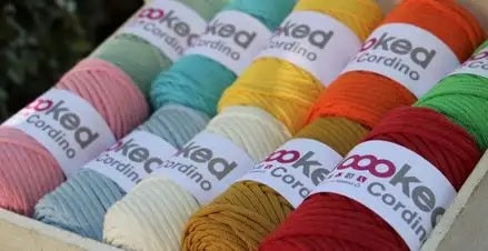 A collection of colorful Hoooked Cordino yarn skeins arranged in a box, with labels showing the brand and yarn type.