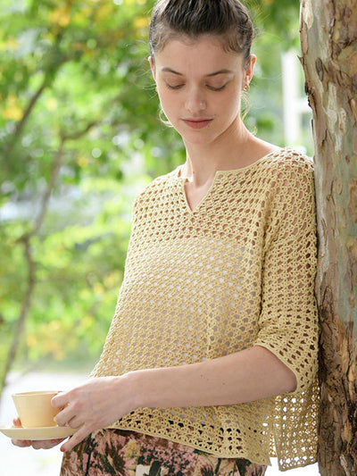 Woman wearing a yellow crochet top holding a cup outdoors.
