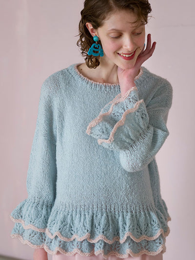 Woman wearing a light blue knitted dress with lace trim against a pink background