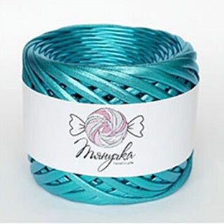 A spool of metallic light blue yarn with a label that has a heart and wings graphic on it, set against a blurred bokeh background.