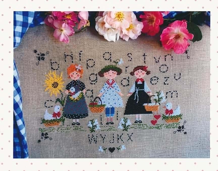 A professional-grade cross-stitch chart by Italian designer Lilli Violette titled 'A Day In The Country.' The high-definition design features a large, horizontally-oriented pastoral scene filled with artisanal motifs such as country houses, blooming gardens, farm animals, and figures enjoying the outdoors.