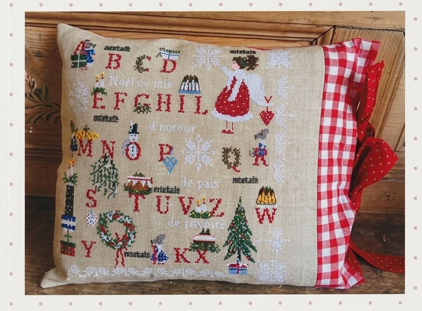 A professional cross-stitch chart by Lilli Violette titled 'Noël de Joie.' This high-definition alphabet sampler is packed with festive motifs, including a grand Christmas tree, a lush holiday wreath, colorful presents, and a charming snowman.