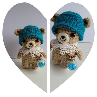 A Crochet teddy bear with a blue knitted hat carrying a glass round bottle filled with blue tiny stars. For sale.  The perfect palm-sized traveling companion made from soft, durable yarn for comfort on long journeys.