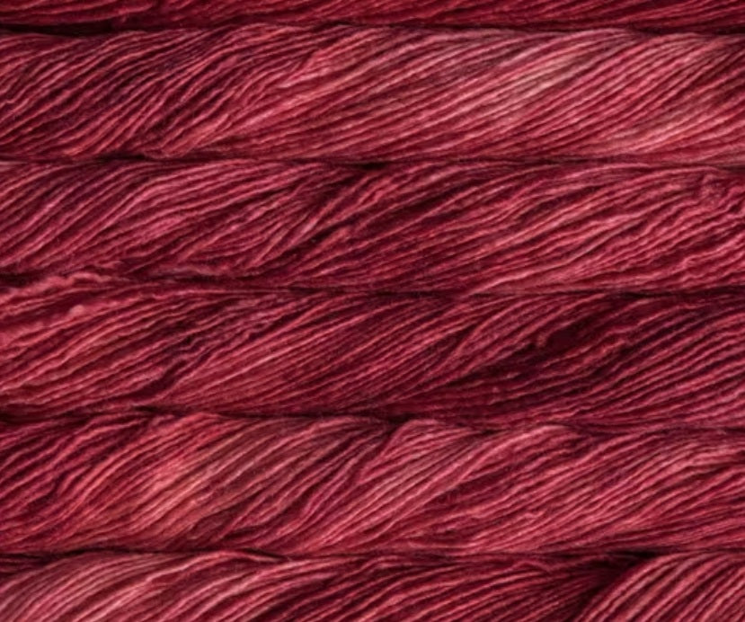 A 50g skein of Malabrigo Silky Merino yarn, featuring a premium 50% silk and 50% merino wool blend in a dk weight for a soft, shimmering finish in Ravelry Red