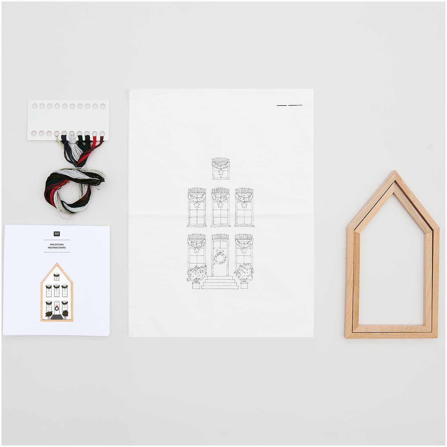 Contents of the Mansion De Noel kit: printed embroidery fabric, colorful cotton threads, needle, and a light wood house-shaped display frame