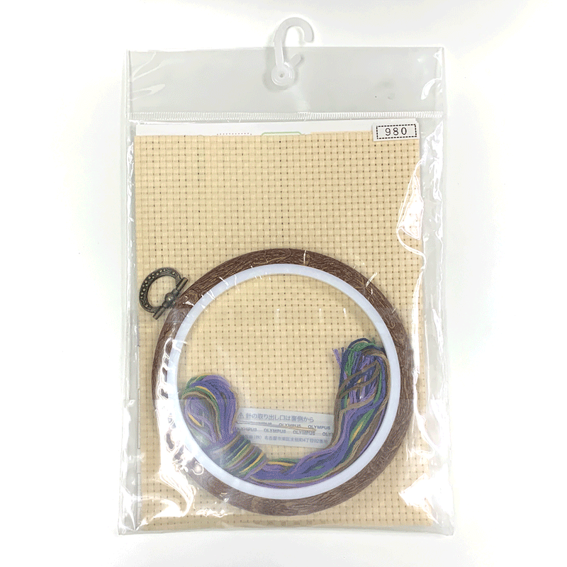 Detailed flat-lay of the Olympus kit: beige Java cross medium-eye cloth, vibrant stranded thread, tapestry needle, and a wood-tone fashionable display hoop
