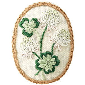 An embroidered brooch kit with a floral design, including pink and green threads on a pink fabric base, with a brooch pin and cotton thread visible.