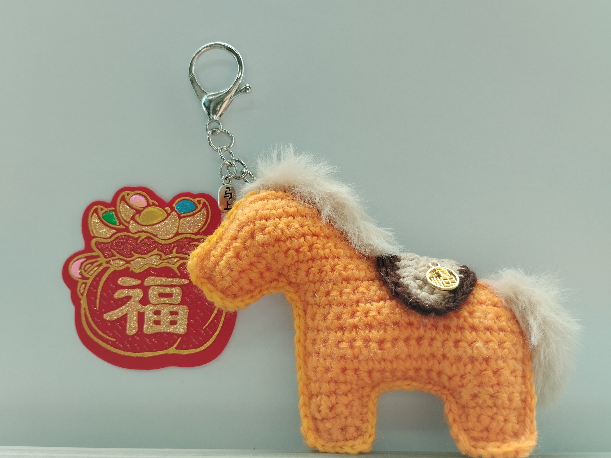 Crocheted horse keychain with a red decorative item on a gray background