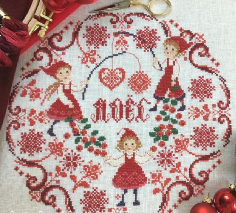 Perrette Samouiloff cross-stitch kit and chart depicting a Christmas wreath with three little elves, heart and star-shaped ornaments, and the word 'Noël' in gothic letters, stitched on a 28 count linen fabric.