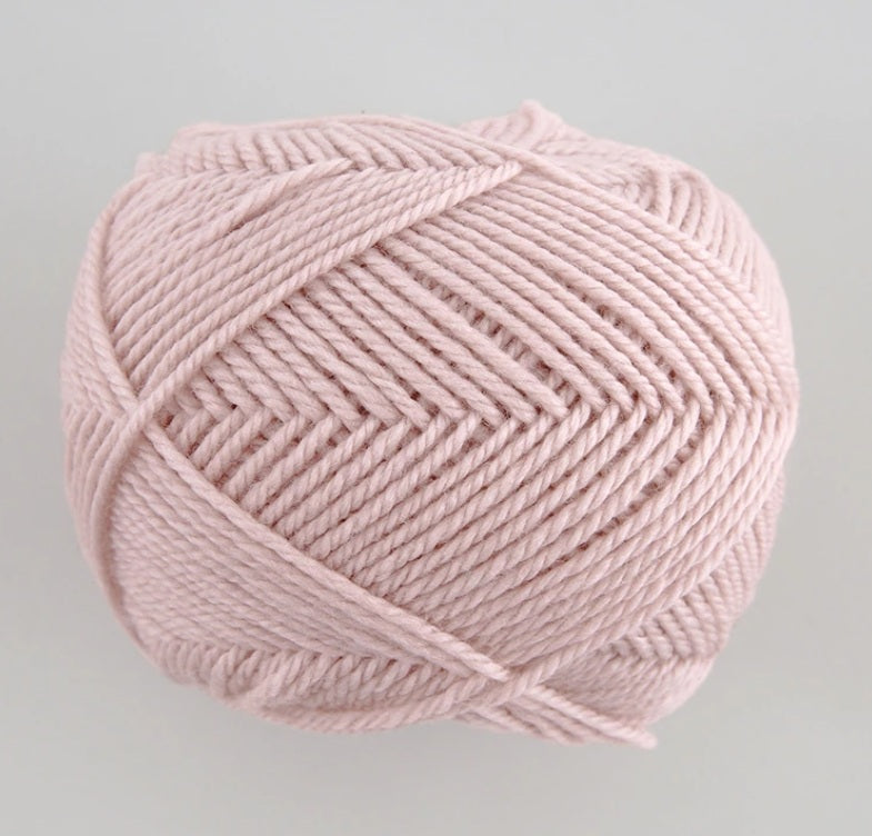 A 30g donut-style ball of Pierrot Fine Merino yarn. The image showcases the smooth, tightly spun plies of 100% Extra Fine Merino wool, reflecting the high-quality Japanese craftsmanship and the soft, matte finish characteristic of premium boutique yarns in baby pink