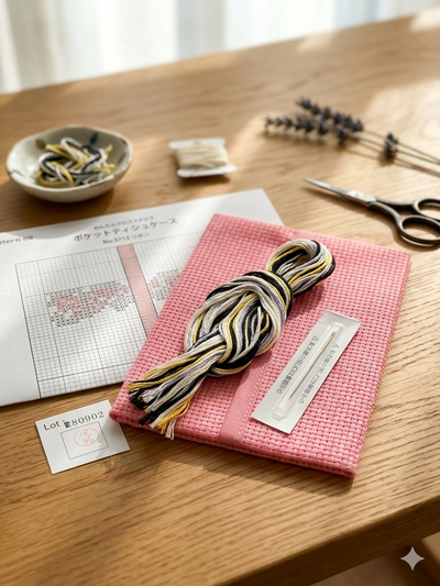 pink fabric with a ruler and a bowl of yarn in the background on a wooden table. cross stitch kit singapore