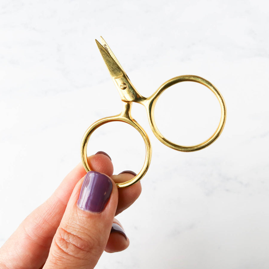 A pair of Putford Primitive miniature scissors featuring distinctively large circular finger holes and short, sharp blades. The scissors are shown in three vintage-inspired colors, highlighting their compact 2.5-inch size and handcrafted 'primitive' aesthetic, perfect for precise thread snipping