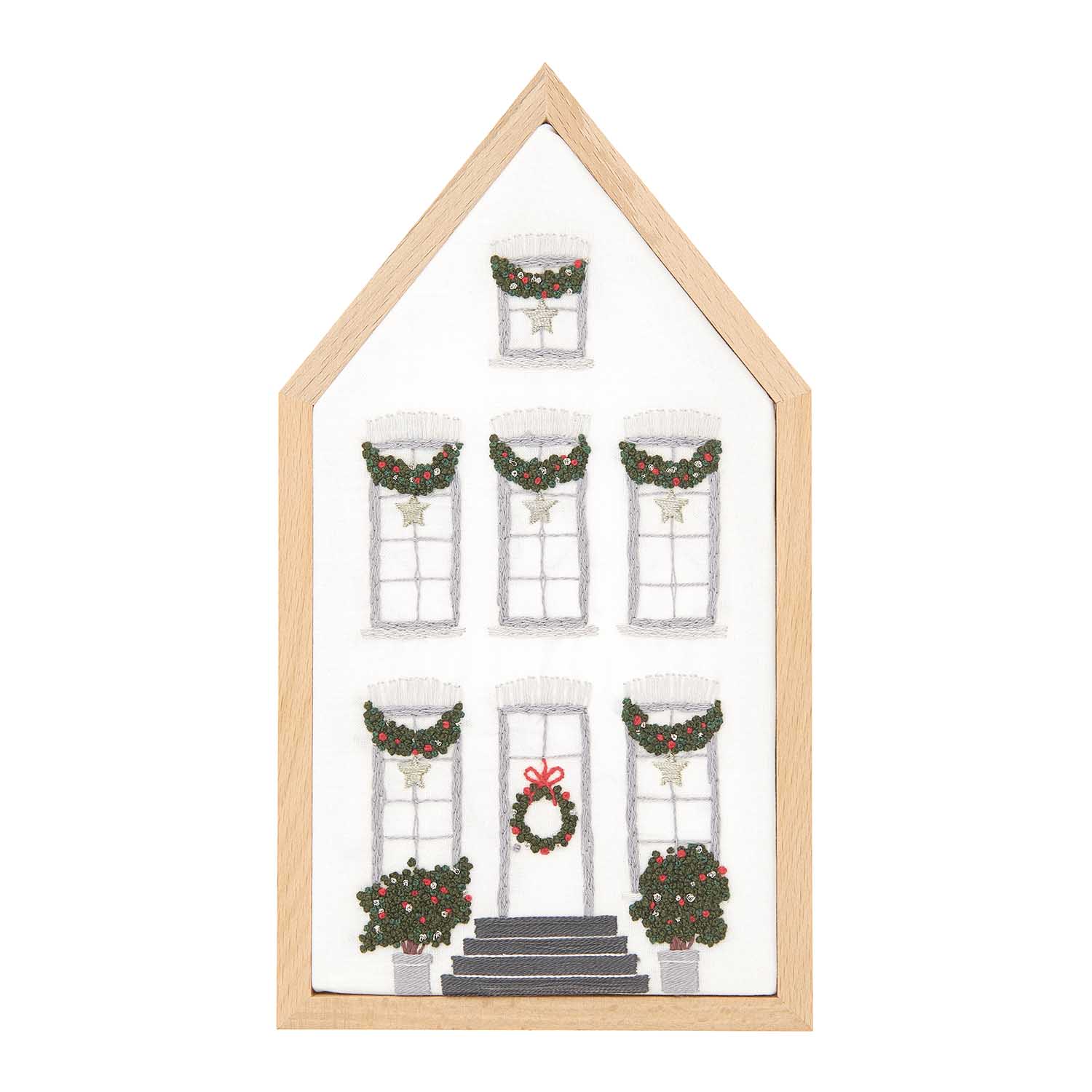 Embroidery kit depicting a white mansion with Christmas decorations, including a garland of stars on the windows and a wreath on the door, framed in a light wooden border.