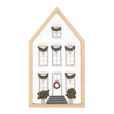 Embroidery kit depicting a white mansion with Christmas decorations, including a garland of stars on the windows and a wreath on the door, framed in a light wooden border.
