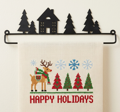 Cross-stitched towel with Christmas design featuring a reindeer, trees, and 'Happy Holidays' text, hanging on a black metal rack.