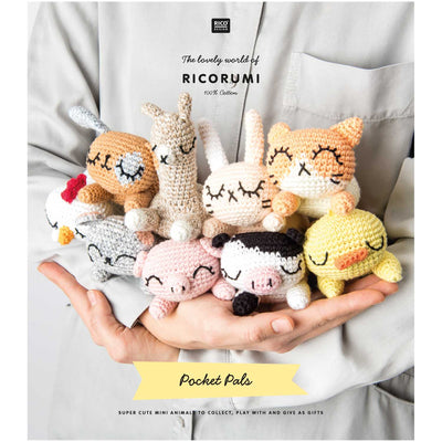 Ricorumi Pocket Pal instruction book with easy-to-follow patterns for pocket-sized crochet toys; an ideal gift for amigurumi beginners. A group shot of the 9 finished Pocket Pals, including the llama, cow, and cat, arranged on a desk as cute companions