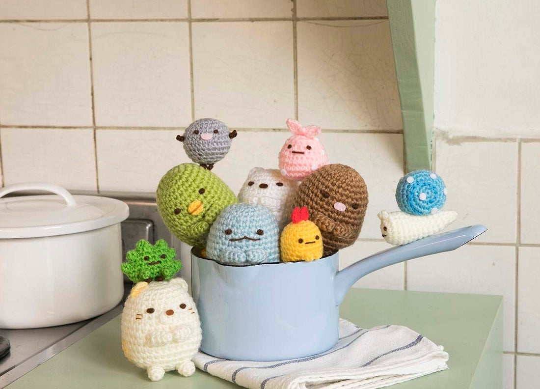 A display of finished Sumikko Gurashi crochet characters arranged in a cute 'corner' scene with felt decorations
