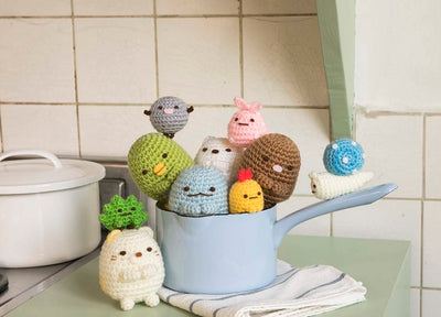 A display of finished Sumikko Gurashi crochet characters arranged in a cute 'corner' scene with felt decorations