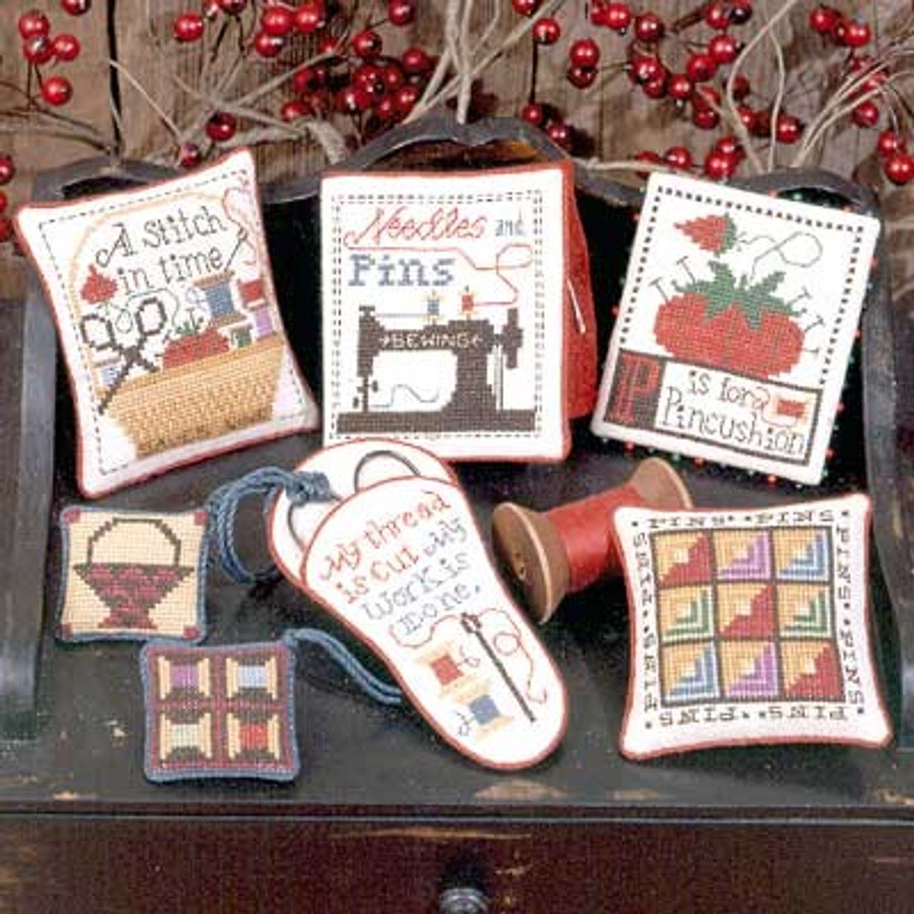 Front cover of the Prairie Schooler Pins and Needles chart featuring multiple primitive-style cross-stitch samplers and sewing accessories.

A collection of cross stitch designs featuring various textiles and needlework themes, such as a pincushion and scissors, from The Prairie Schooler brand.