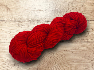 Tomato red yarn on a wooden surface. 100% Superwash Merino, Artisanal luxury yarn for sale