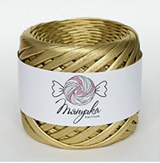 A spool of metallic gold yarn with a label that has a heart and wings graphic on it, set against a blurred bokeh background.
