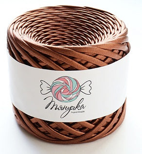 A spool of metallic bronze yarn with a label that has a heart and wings graphic on it, set against a blurred bokeh background.