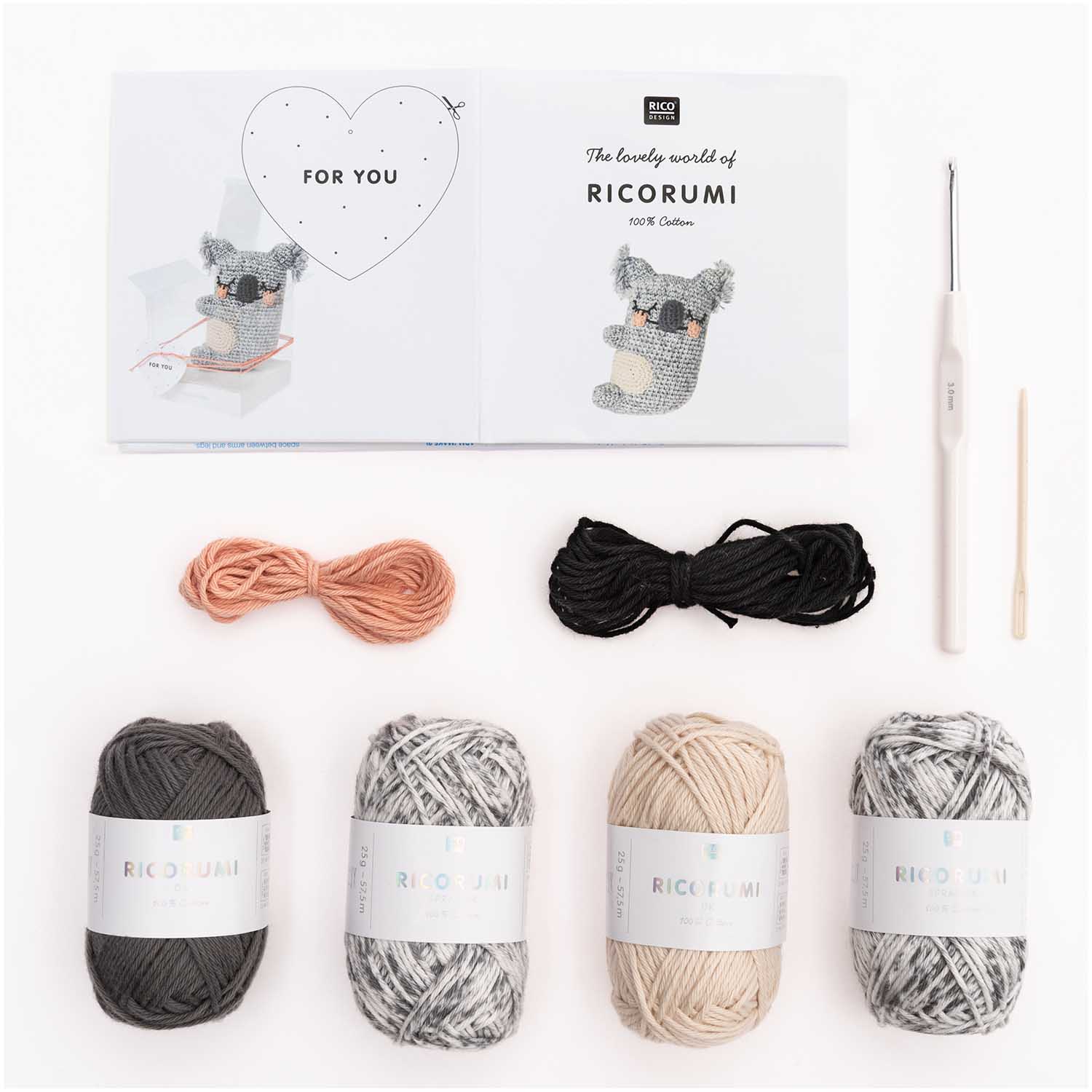 A flat-lay of the kit's contents showing two grey yarn balls, one white yarn ball, a crochet hook, a needle, and the pattern booklet