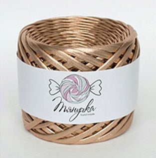 A spool of metallic dark copper yarn with a label that has a heart and wings graphic on it, set against a blurred bokeh background.